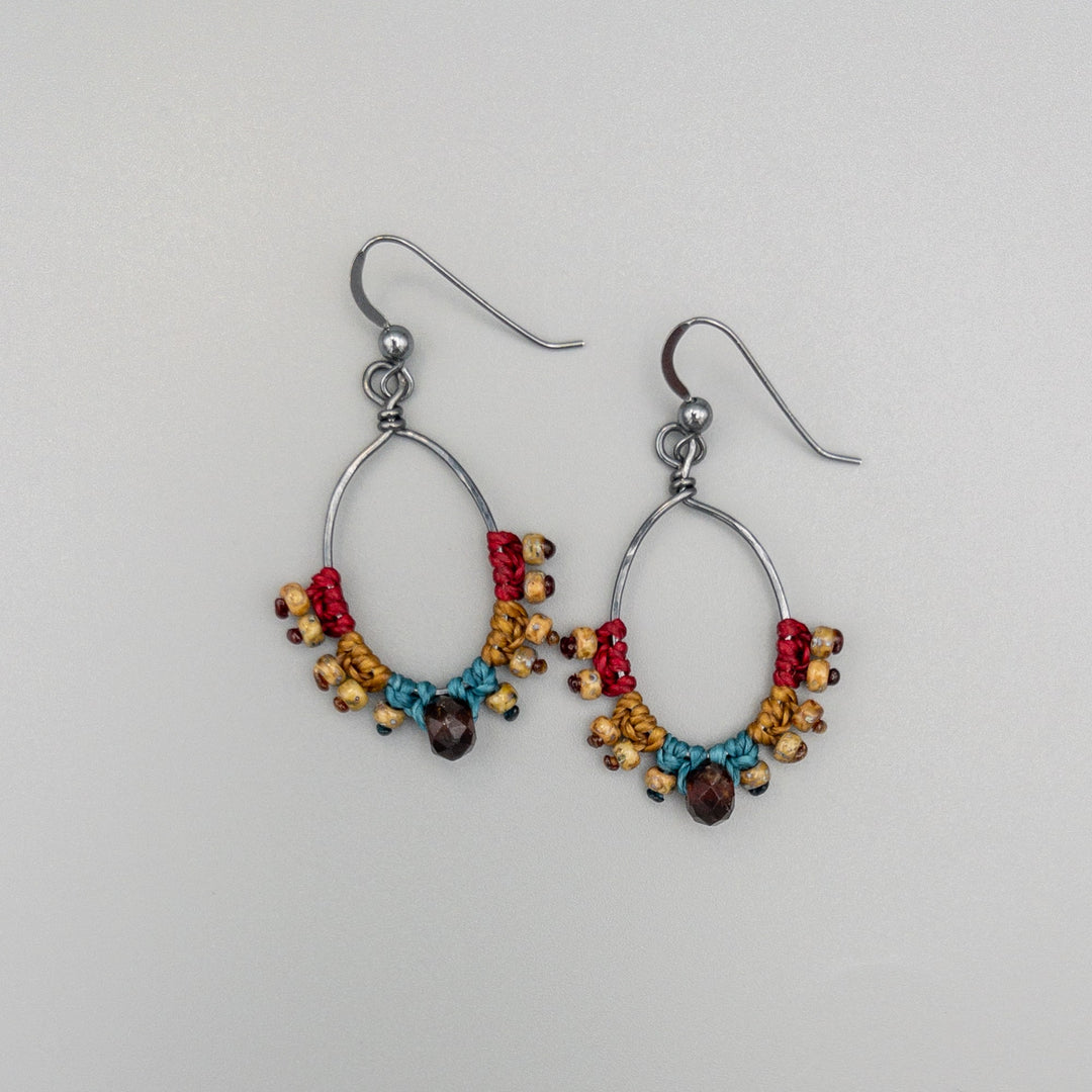 handmade macrame hoop earrings with garnet bead on a gray background
