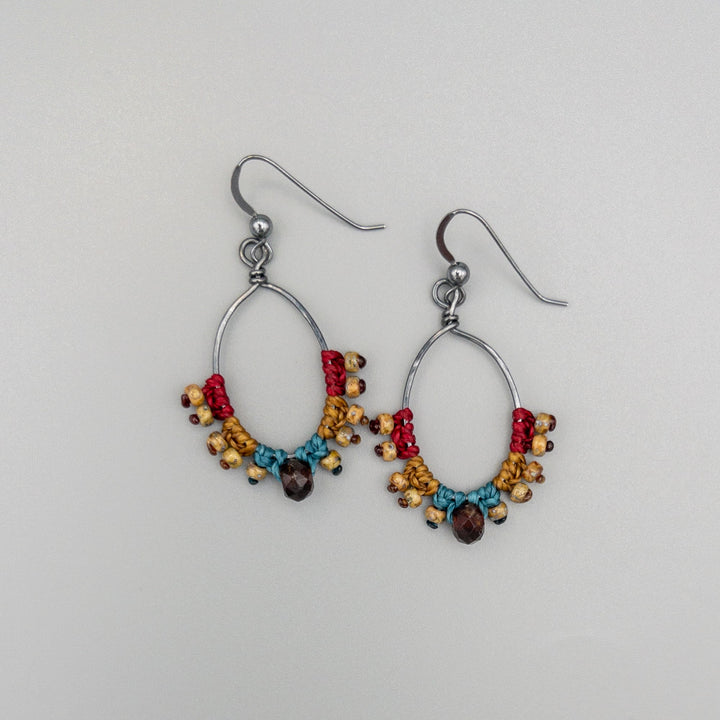 handmade macrame hoop earrings with garnet bead on a gray background