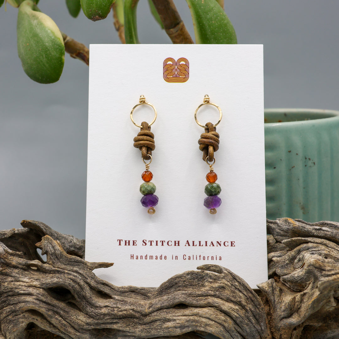 handmade amethyst, green garnet, and hessonite leather and gold fill earrings on a white display card