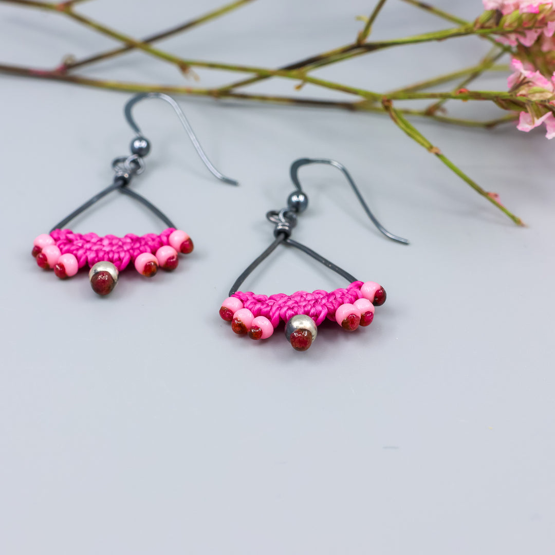detail view of handmade oxidized sterling silver triangle hoop earrings with bright pink macrame