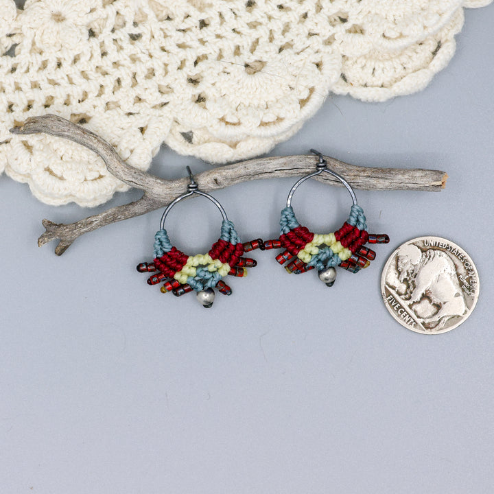 handmade macrame stud earrings in blue, deep red, and pale yellow with oxidized sterling silver metal with a coin for size comparison