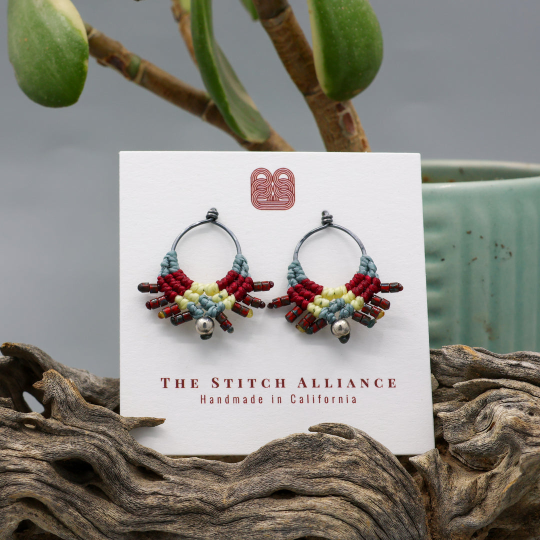 handmade macrame stud earrings in blue, deep red, and pale yellow with oxidized sterling silver metal on a white display card