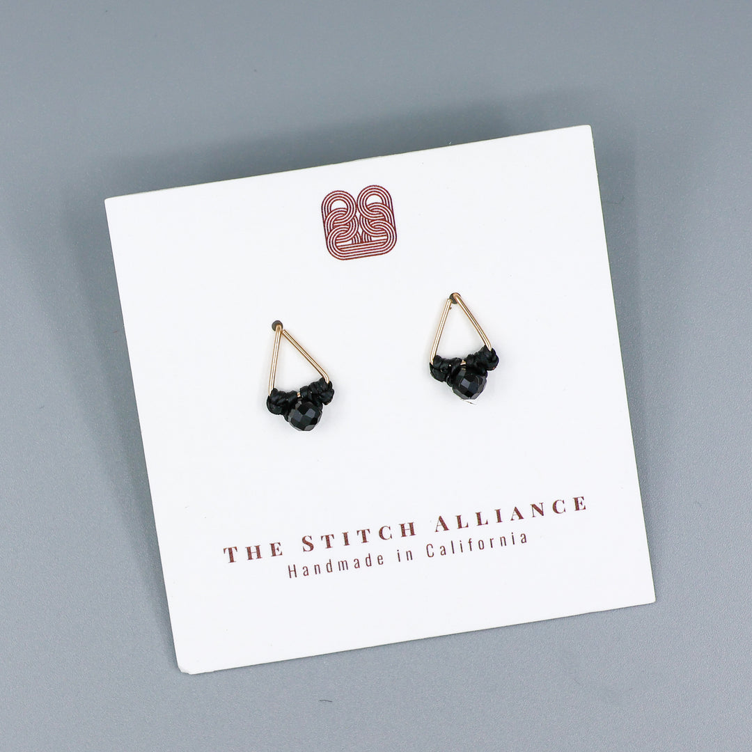 handmade triangle shaped earrings in gold fill with a black spinel bead on a white card and gray backgound
