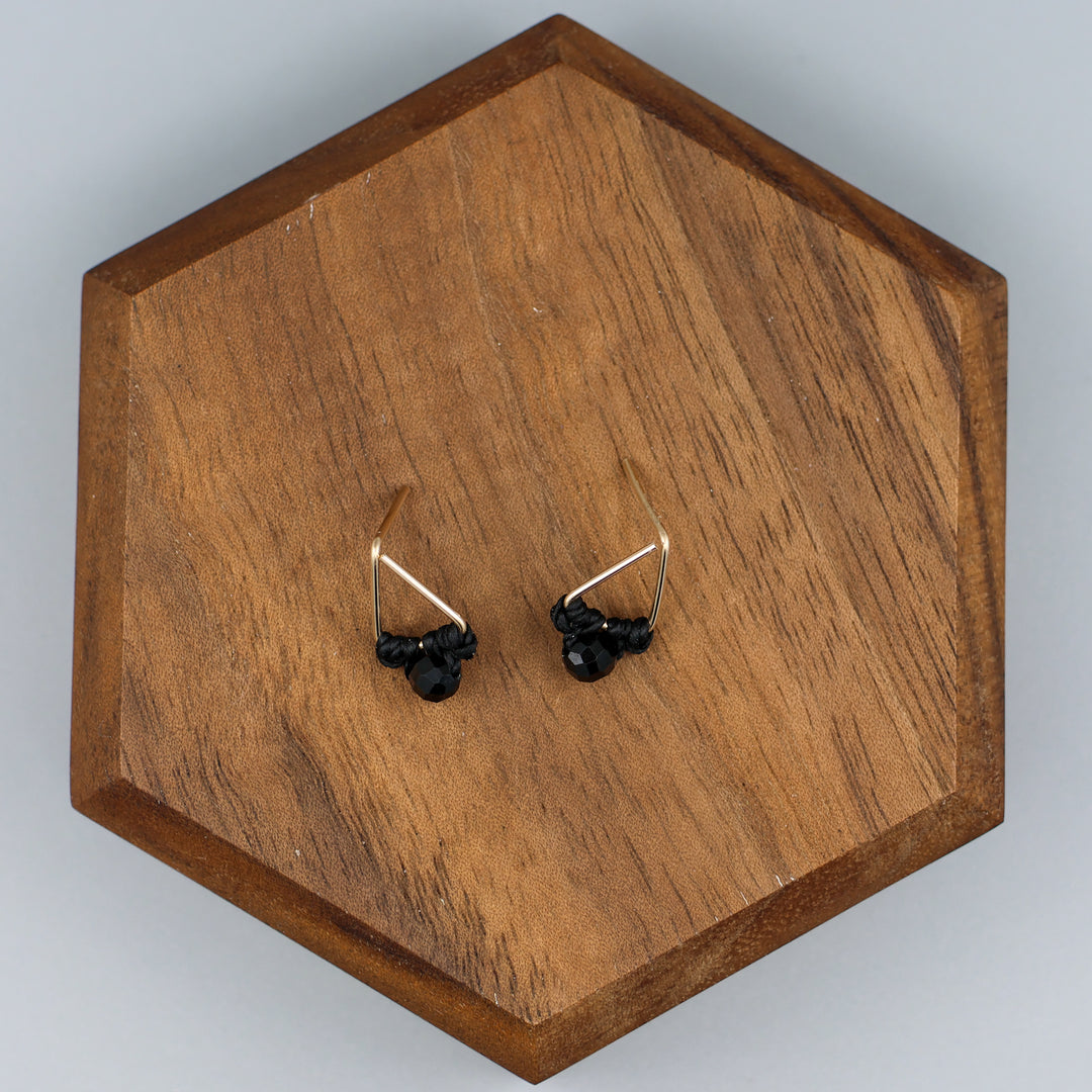 handmade triangle shaped earrings in gold fill with a black spinel bead on a wood display