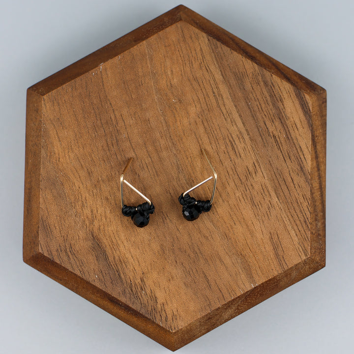 handmade triangle shaped earrings in gold fill with a black spinel bead on a wood display