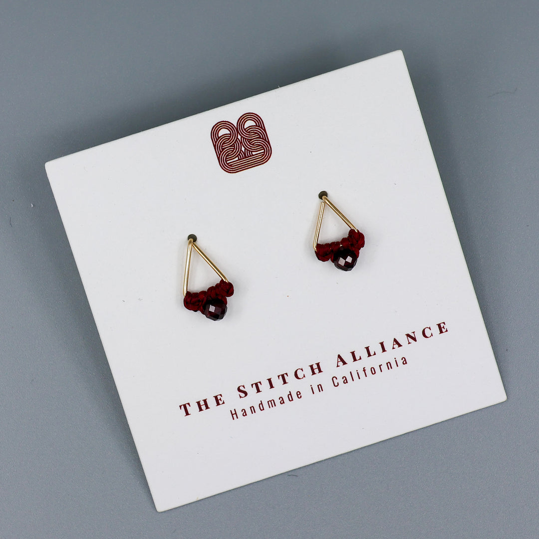 handmade gold filled triangle stud earrings with garnet beads on a white card with gray background