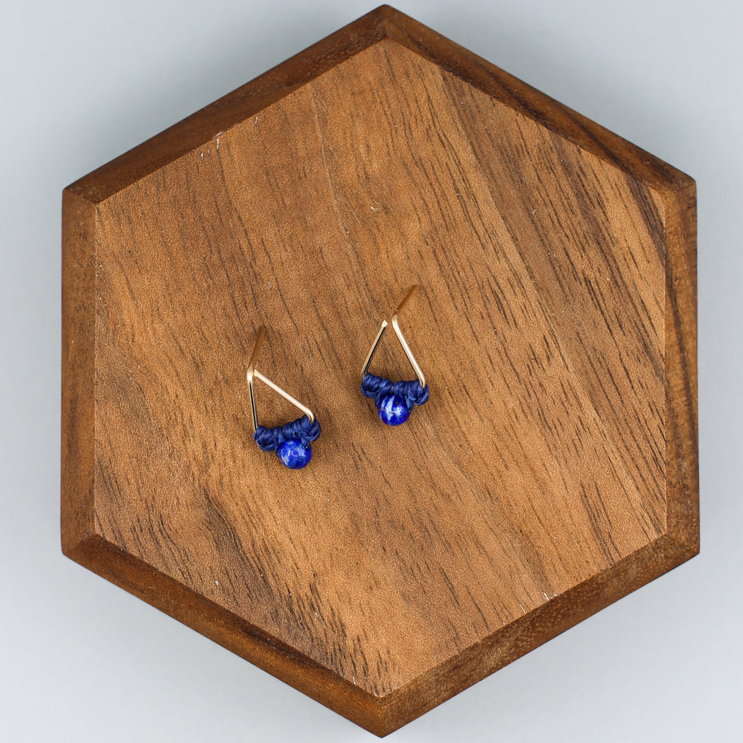 handmade triangle shaped earrings in gold fill with a lapis lazuli bead on a wood display