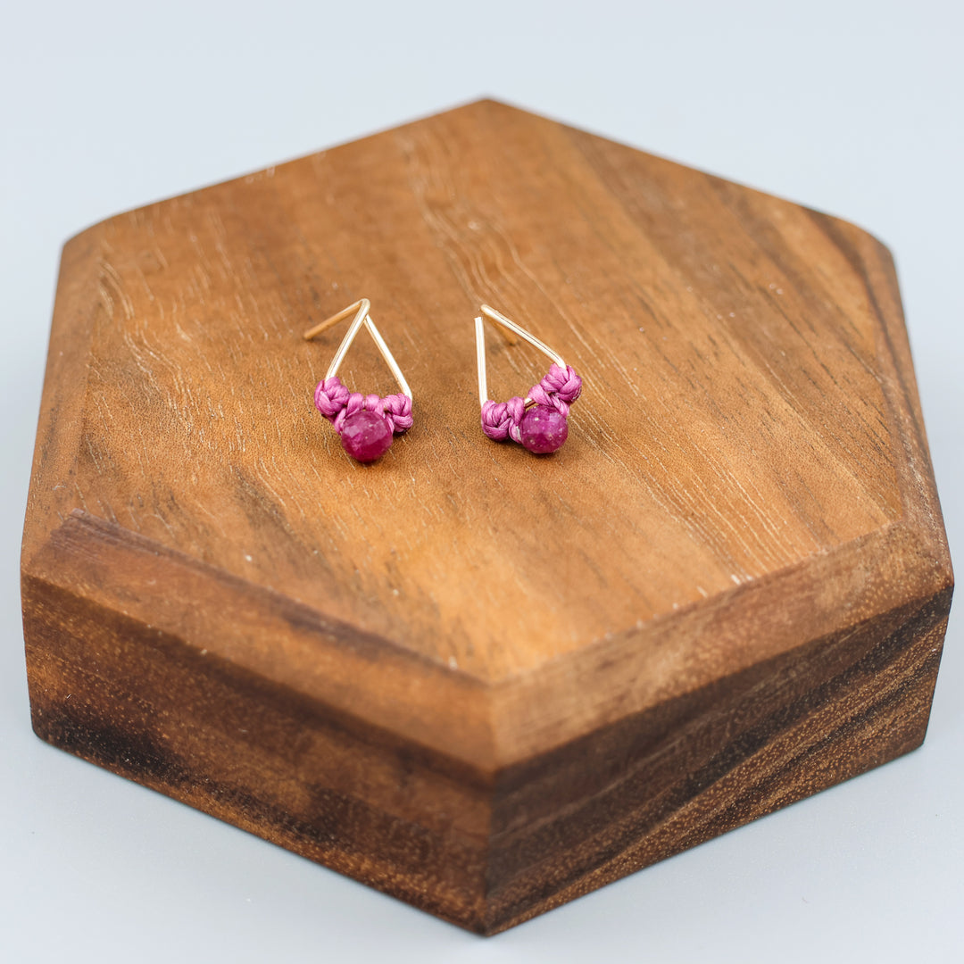 handmade gold filled triangle stud earrings with ruby beads  on a wood display