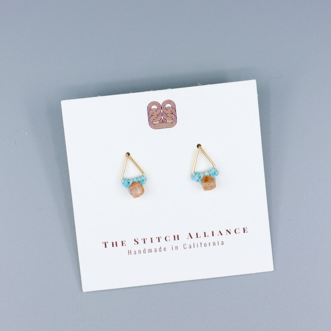 handmade triangle shaped earrings in gold fill with a sunstone bead on a white card with gray background