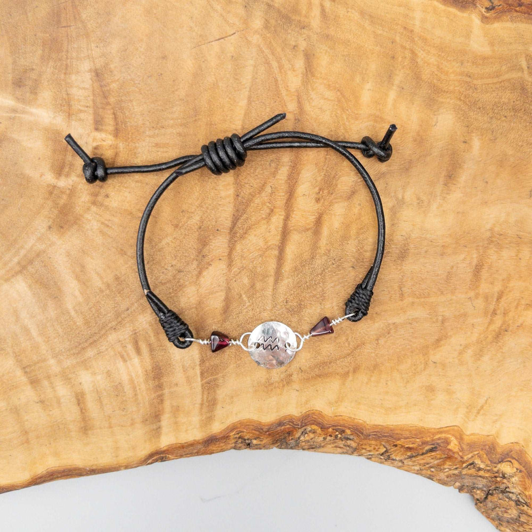 Aquarius bracelet with garnet beads and hand-stamped Aquarius symbol on sterling silver shown on a wood background