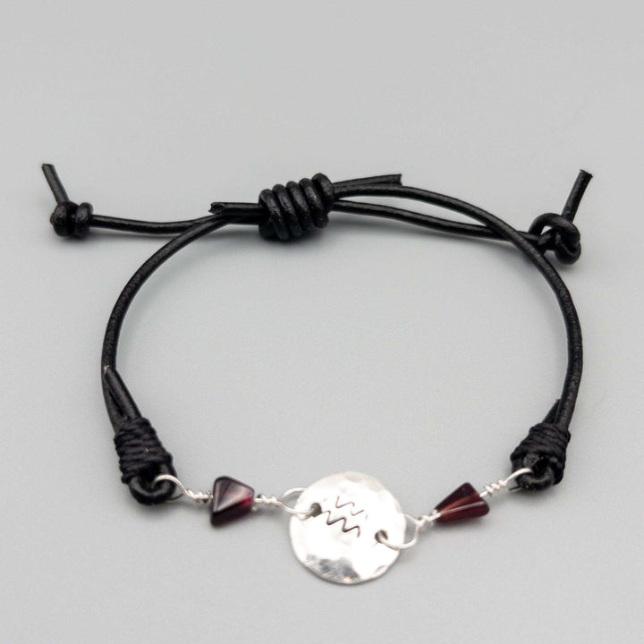 Aquarius bracelet with garnet beads and hand-stamped Aquarius symbol on sterling silver shown on a gray background