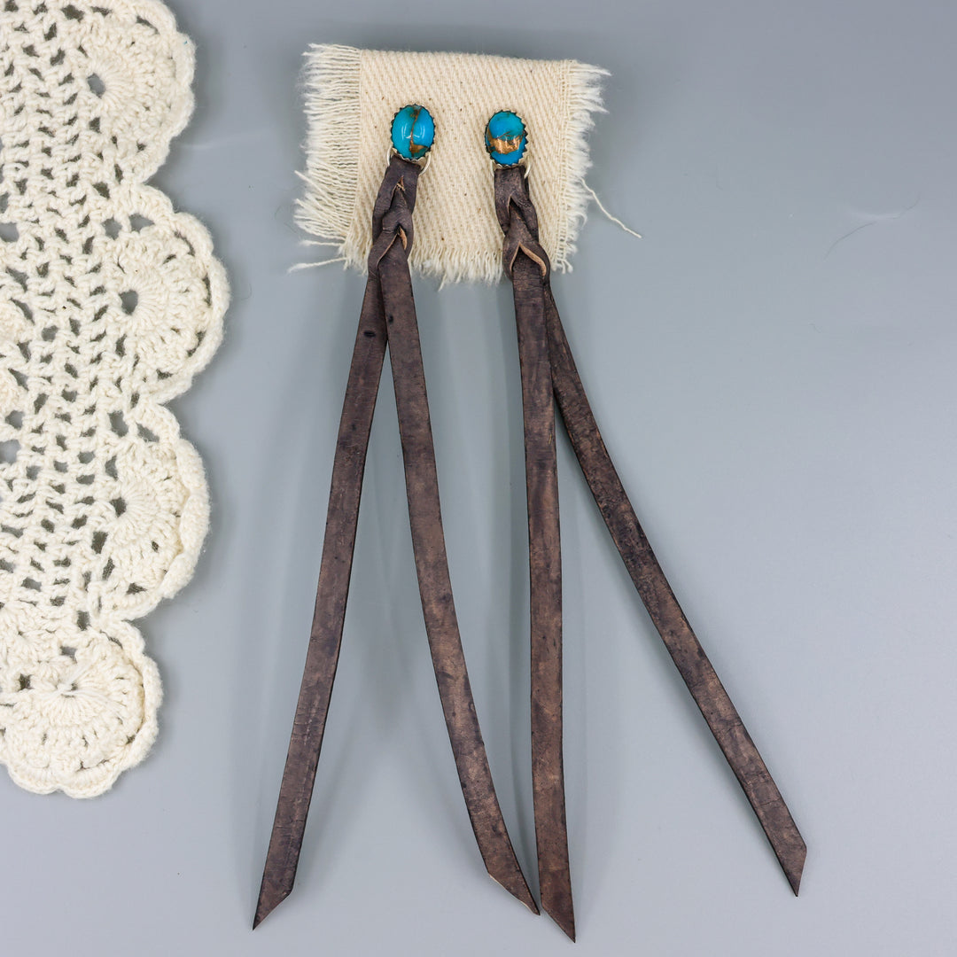 handmade turquoise earrings with distressed black leather fringe on a gray background
