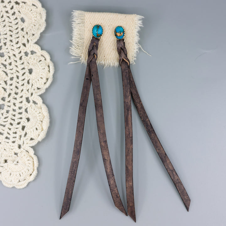 handmade turquoise earrings with distressed black leather fringe on a gray background
