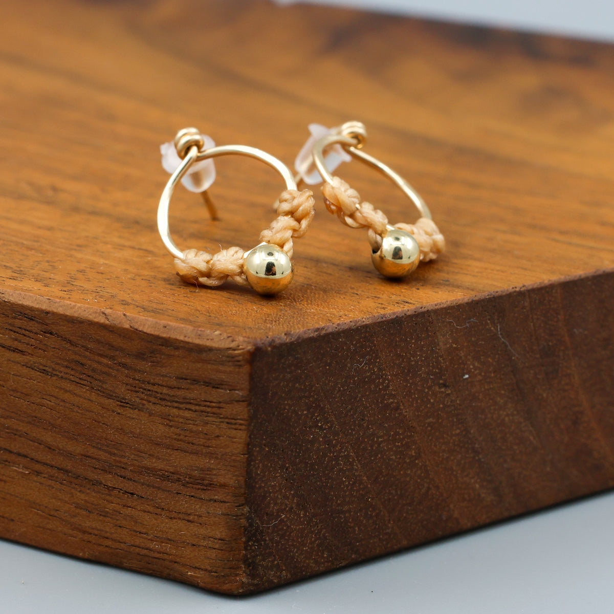 handmade gold macrame stud earrings on a wood display