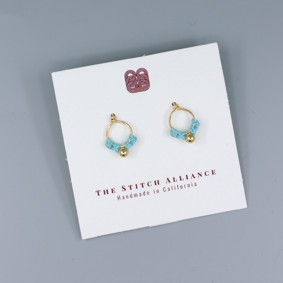 small, handmade gold macrame earrings in blue on a white card