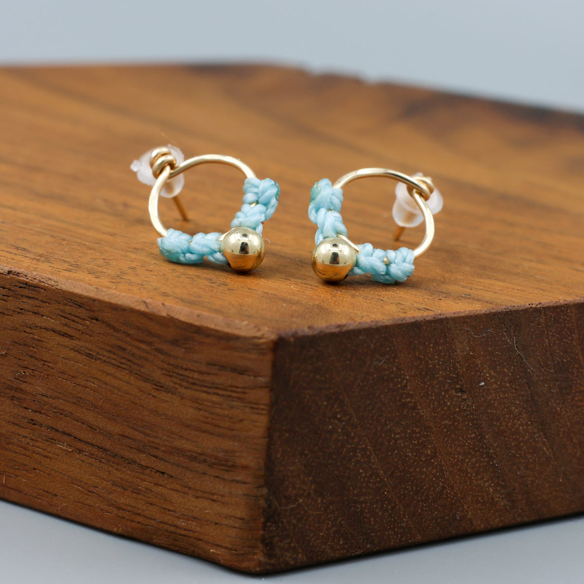 small, handmade gold macrame earrings in blue on a wood display