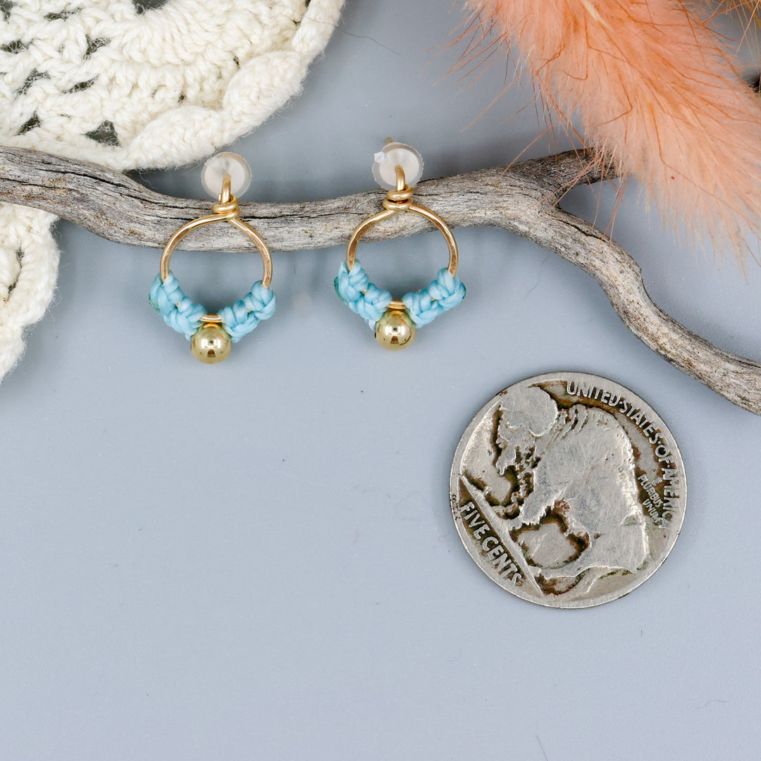 small, handmade gold macrame earrings in blue with a nickel for size comparison