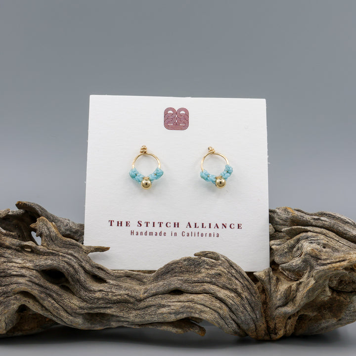 small, handmade gold macrame earrings in blue on a white card