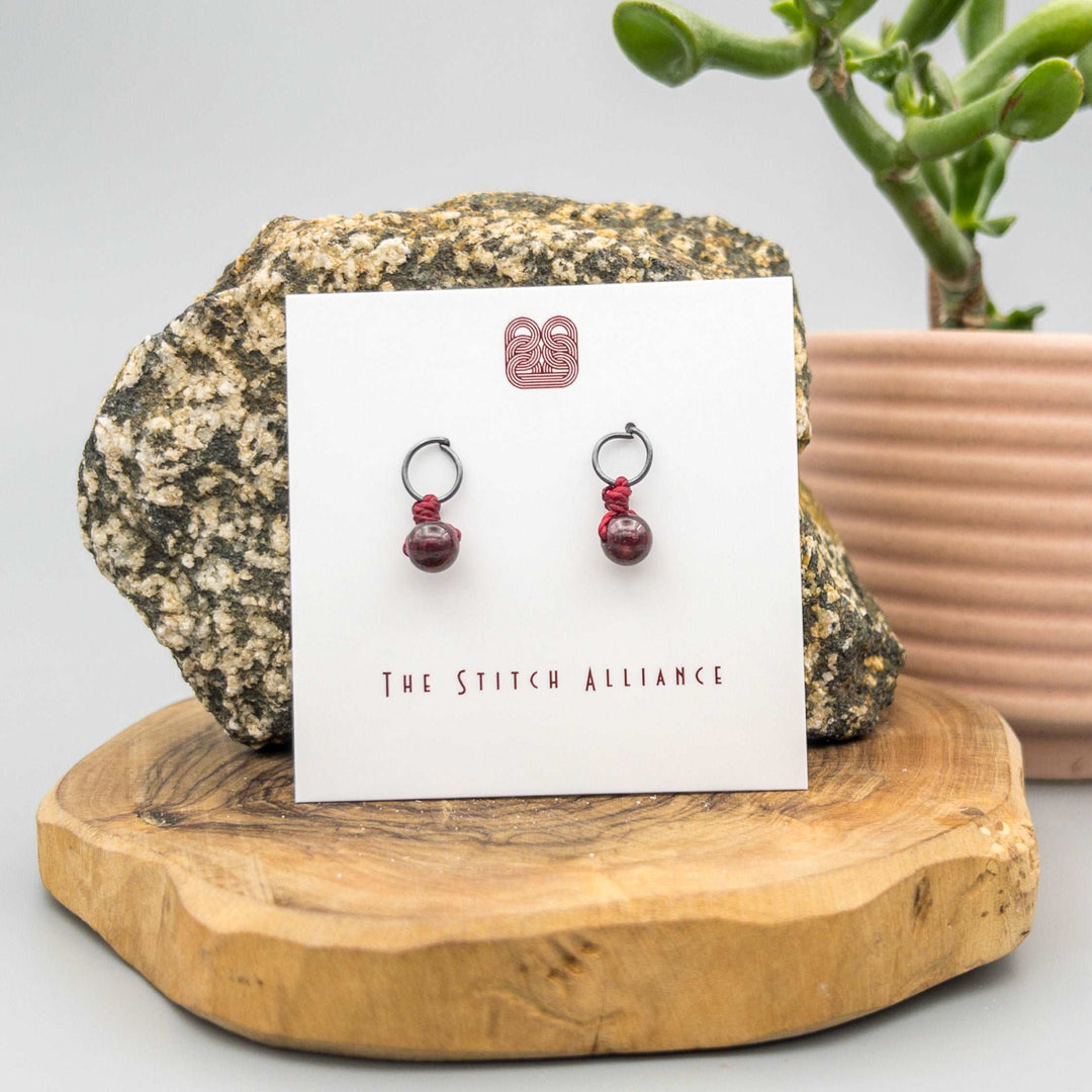 circle post style earrings handcrafted with oxidized sterling silver and a 6mm garnet bead on a white background