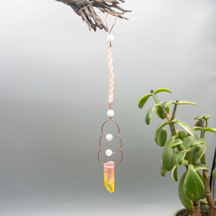 copper, moonstone, and crystal suncatcher made with macrame hanging on a gray background