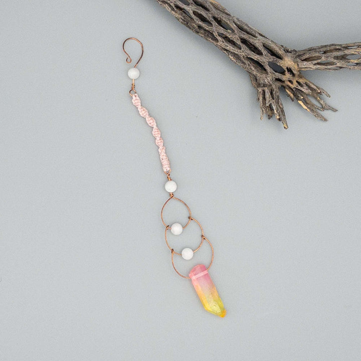 copper, moonstone, and crystal suncatcher made with macrame shown flat on a gray background