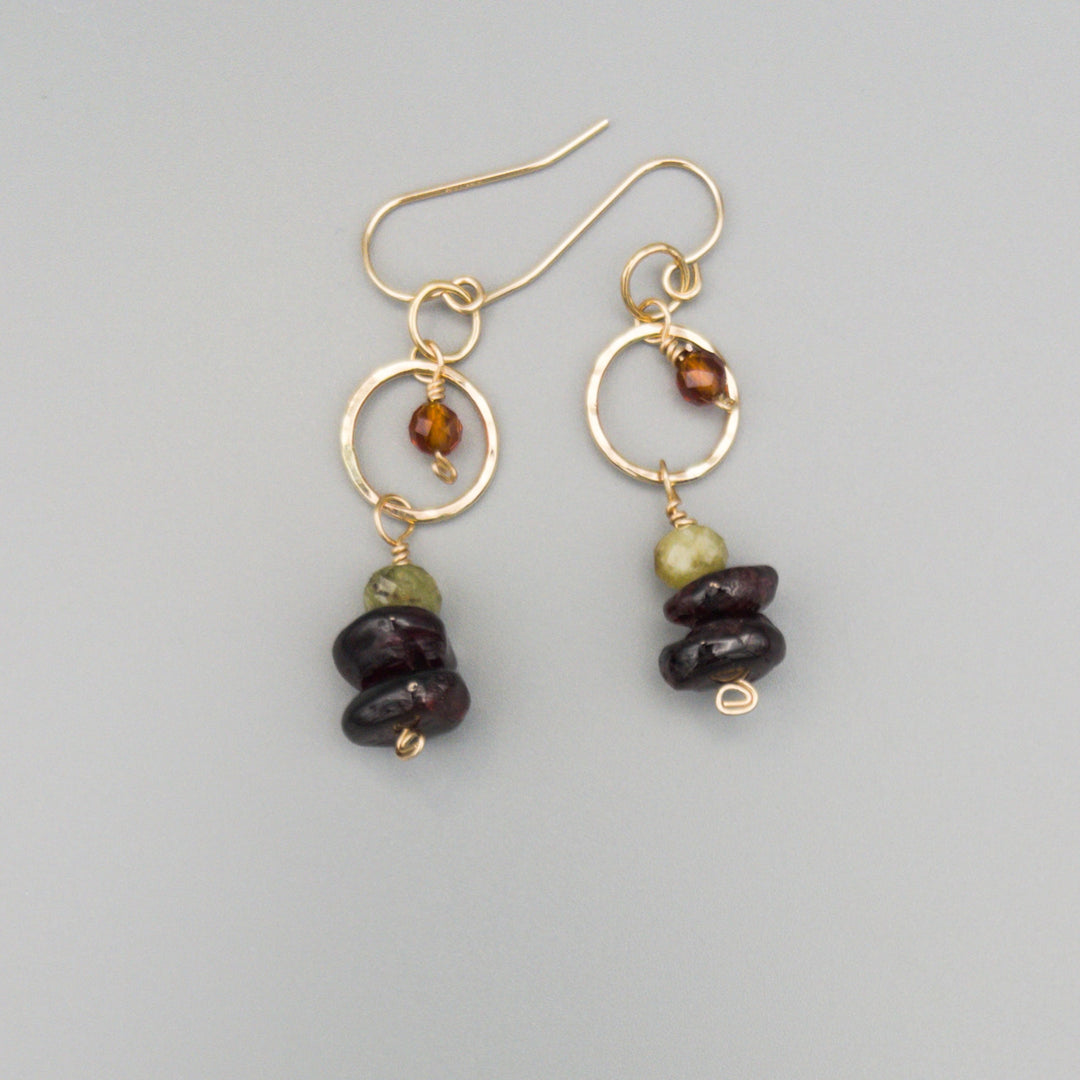 Garnet, green garnet, and hessonite gold filled dangle earrings on a gray background