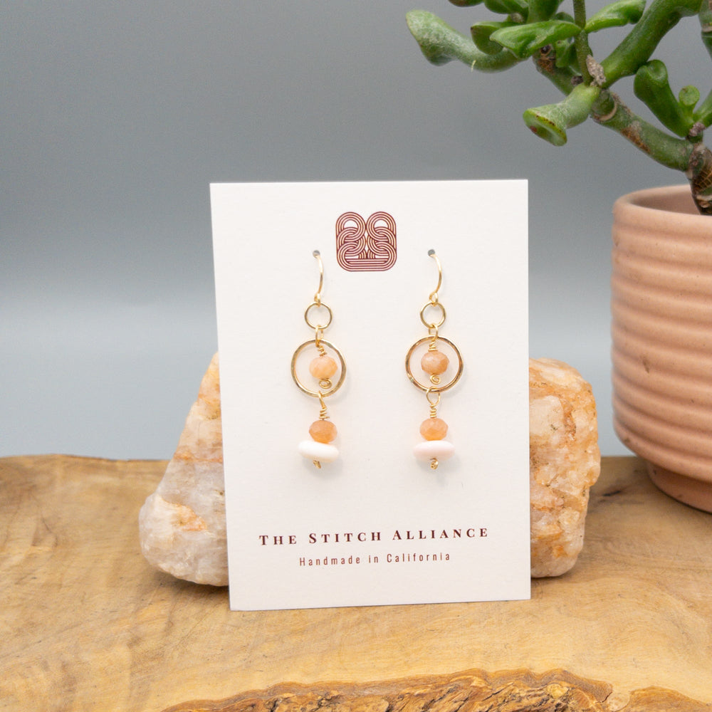 Gold fill, peach moonstone, and queen conch shell handmade earrings on a white card