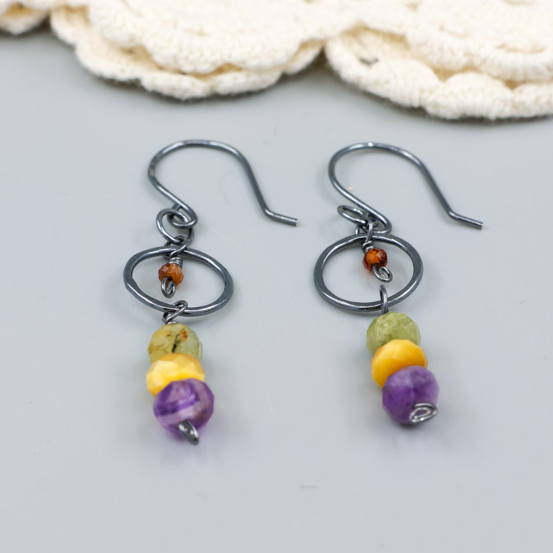 handmade oxidized sterling silver, amethyst, golden tigers eye, green garnet, and hessonite dangle earrings on a gray background