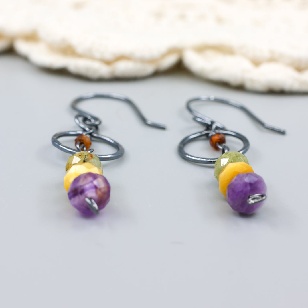 close up view of handmade oxidized sterling silver, amethyst, golden tigers eye, green garnet, and hessonite dangle earrings