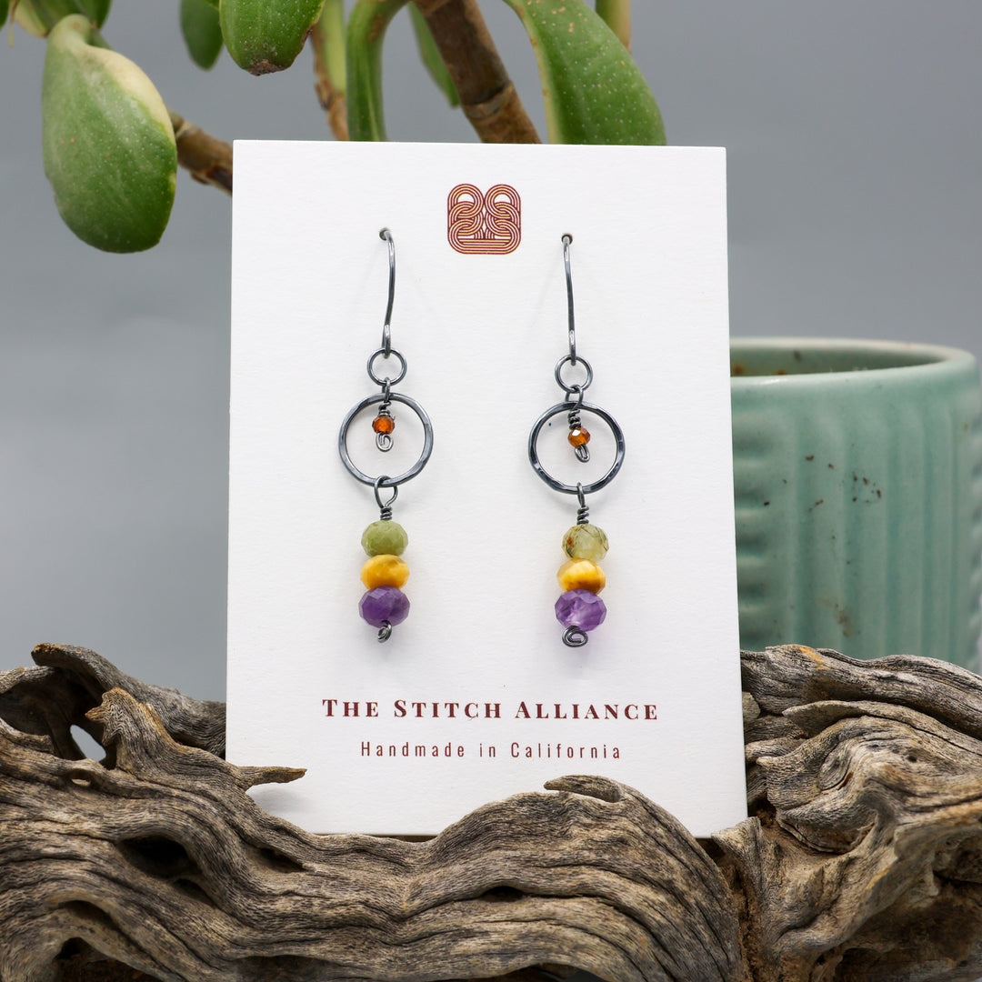 handmade oxidized sterling silver, amethyst, golden tigers eye, green garnet, and hessonite dangle earrings on a white display card