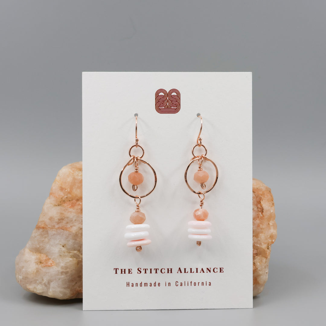 queen conch and peach moonstone rose gold dangle earrings on a white card