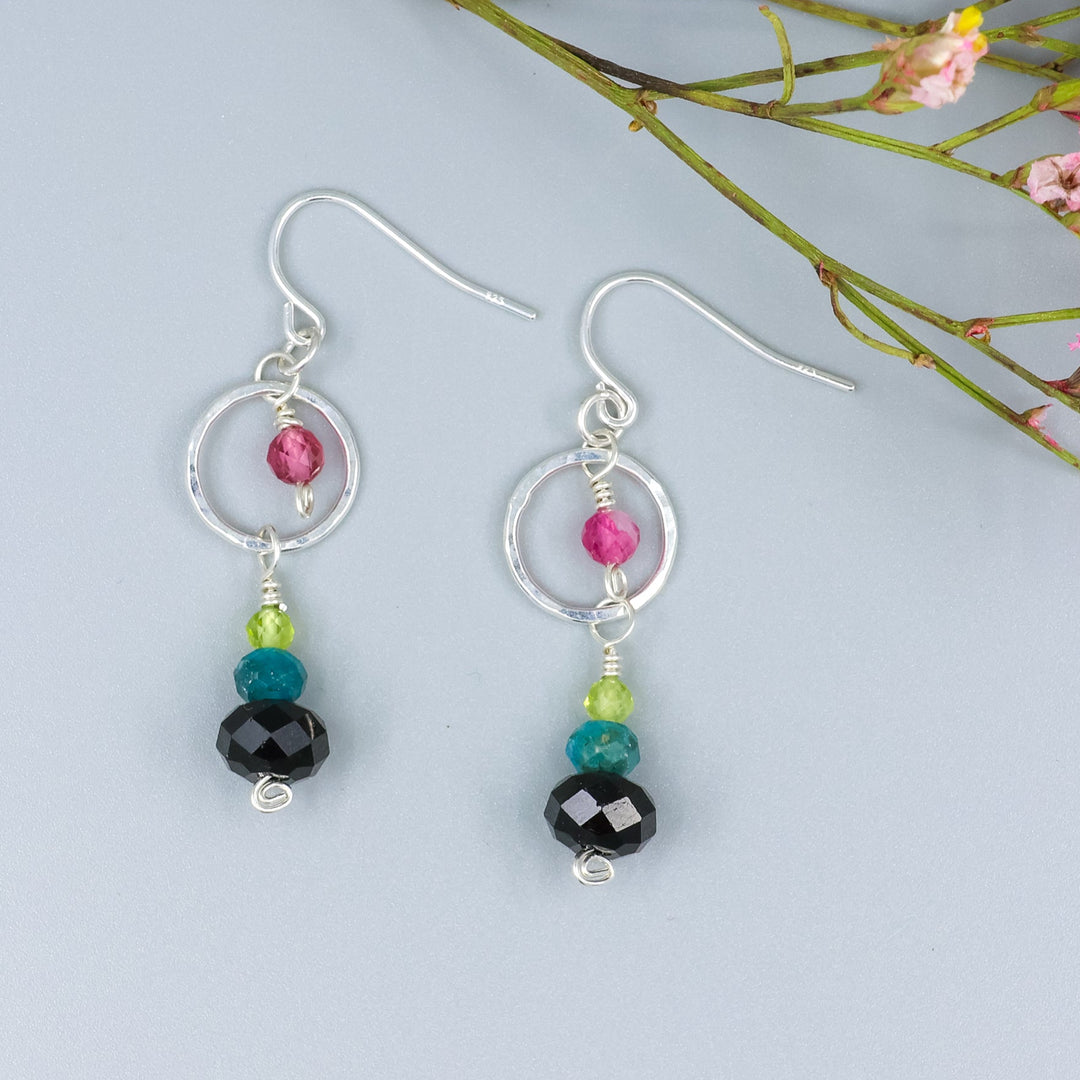 overhead view of handmade gemstone and sterling silver dangle earrings with black tourmaline, blue apatite, peridot, and pink tourmaline