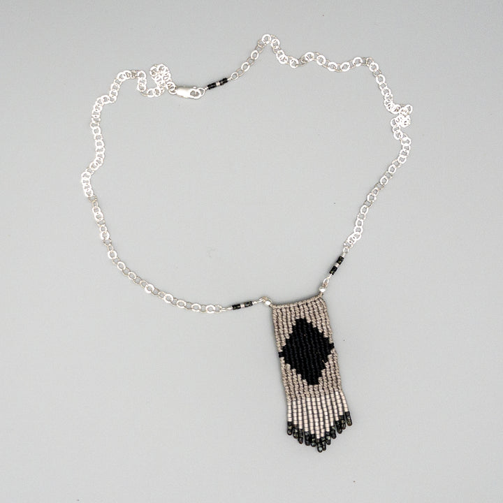 black and gray macrame necklace with seed bead fringe and sterling silver chain on gray background