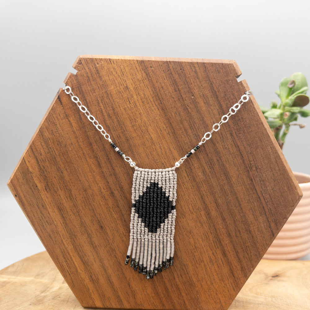 black and gray macrame necklace with seed bead fringe and sterling silver chain on wood background