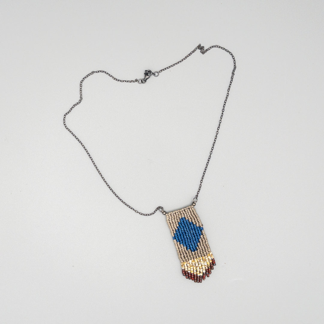Handwoven four elements macrame necklace in blue and tan with tan and red seed bead fringe on a gray background