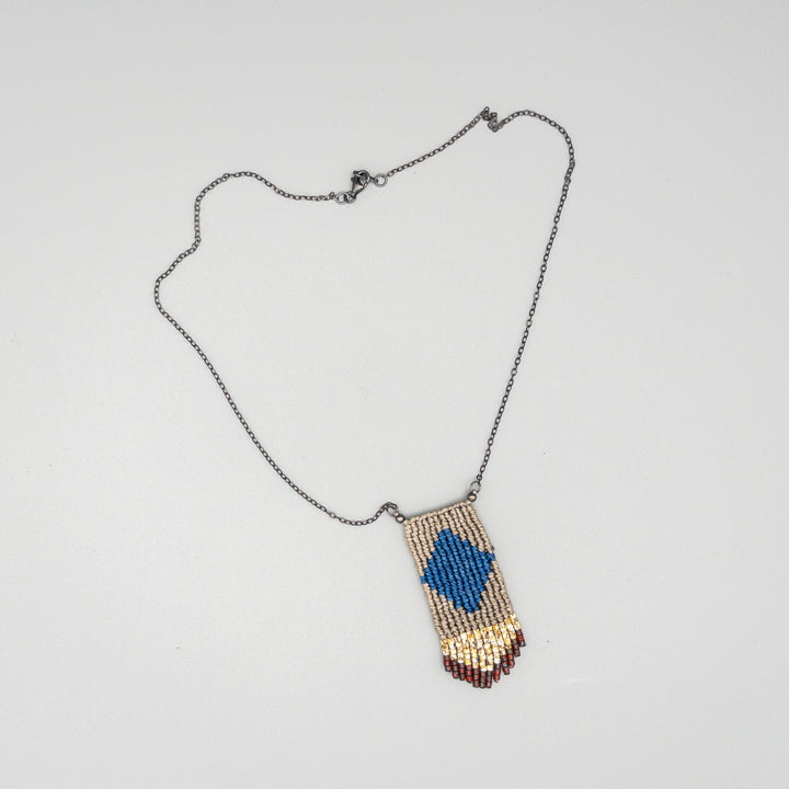 Handwoven four elements macrame necklace in blue and tan with tan and red seed bead fringe on a gray background