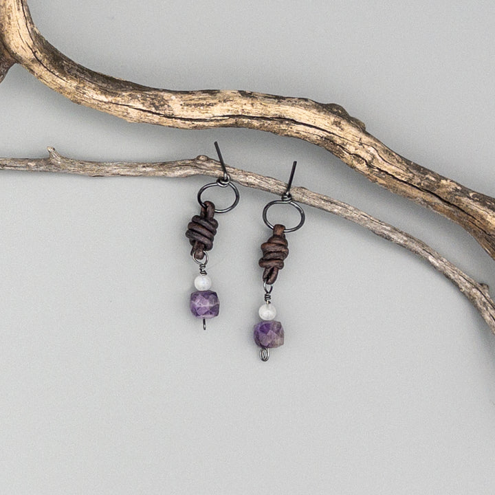 amethyst and moonstone oxidized sterling silver earrings with leather detail on a gray background