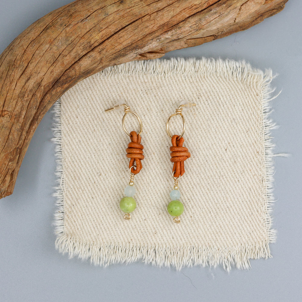 handmade peridot, aquamarine, and leather gold filled earrings on an off white background