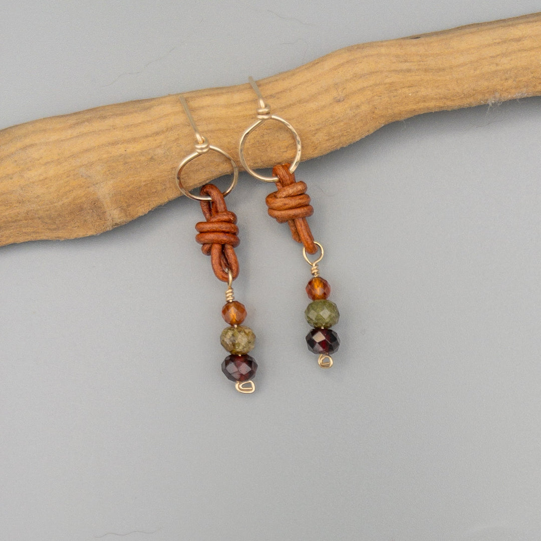 handmade garnet, green garnet, and hessonite gold filled earring with leather on a gray background