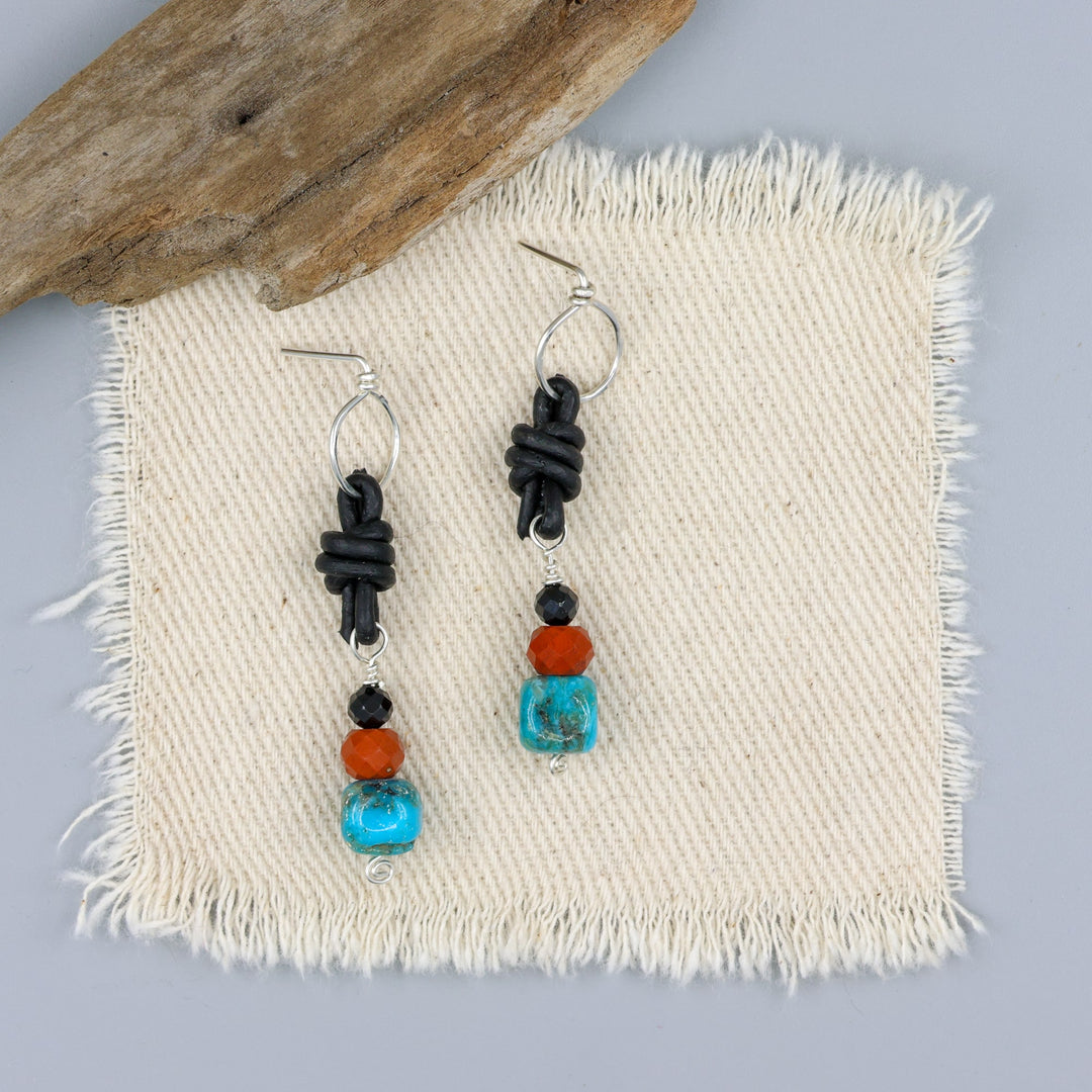 turquoise, poppy jasper, and spinel leather knotted earrings with sterling silver on an off white background