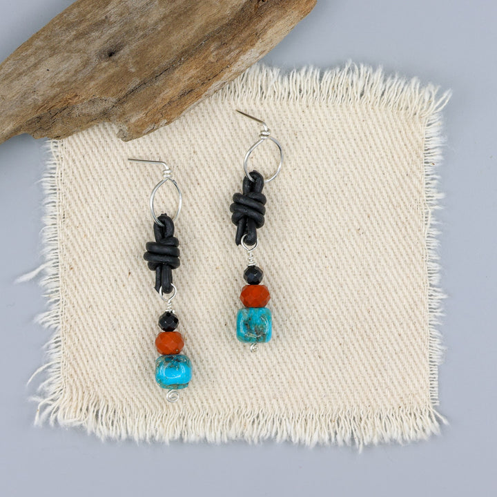 turquoise, poppy jasper, and spinel leather knotted earrings with sterling silver on an off white background