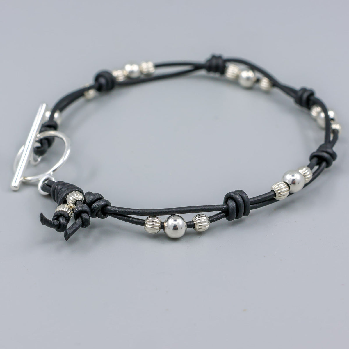 handmade sterling silver and black leather bracelet on a gray background