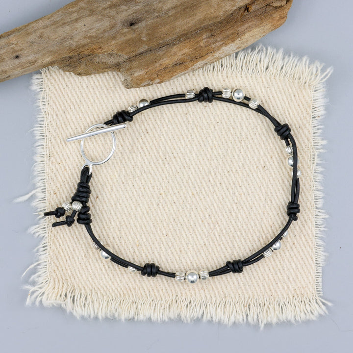 handmade sterling silver and black leather bracelet on an off white background