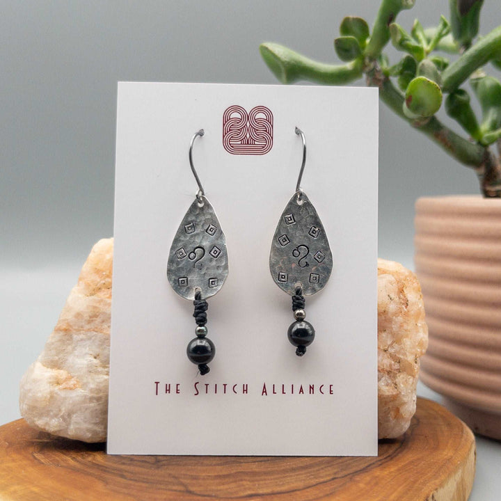 Hand-stamped Leo earrings with black spinel beads on a white card