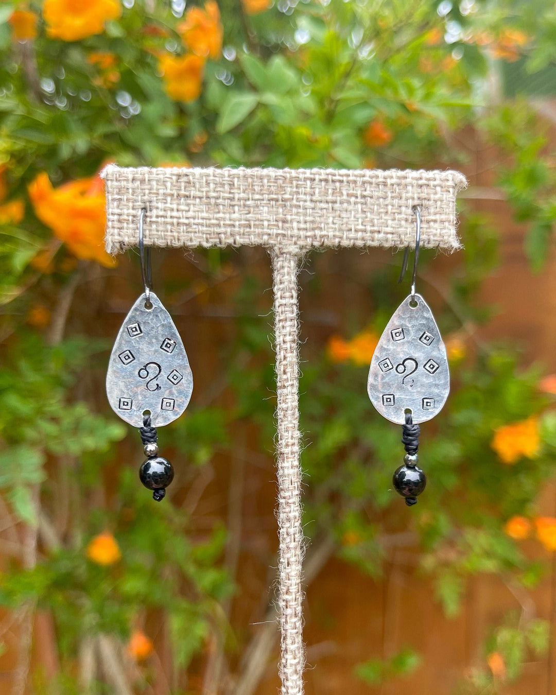 Hand-stamped Leo earrings with black spinel beads shown outdoors