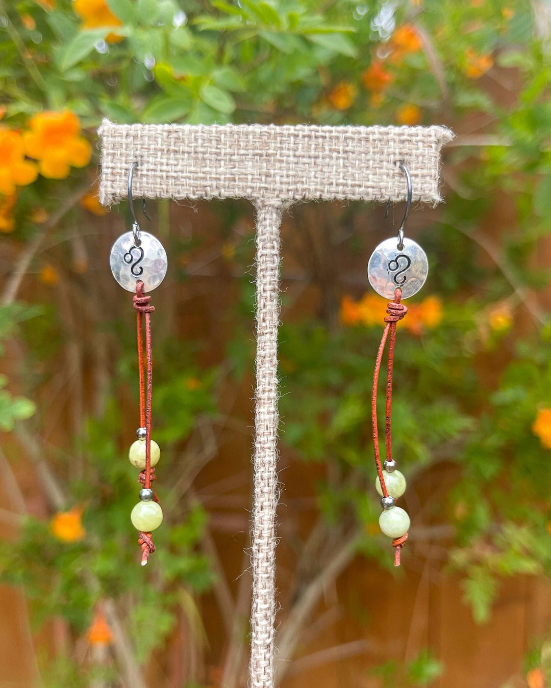Sterling silver Leo stamped earrings with peridot beads on long leather cord shown outdoors