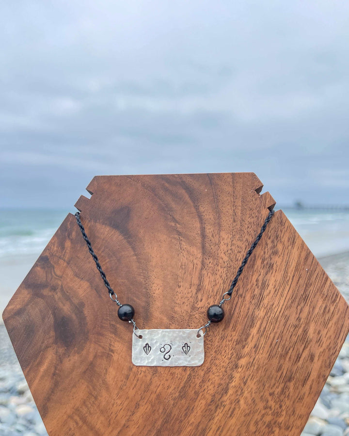 Leo stamped sterling silver necklace with black spinel beads at the beach