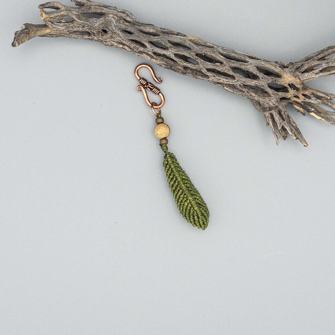 macrame feather charm on copper clip with lava bead diffuser in olive green on gray background