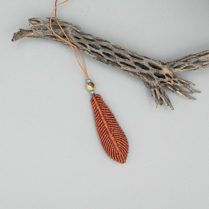 large terracotta macrame feather on gray background