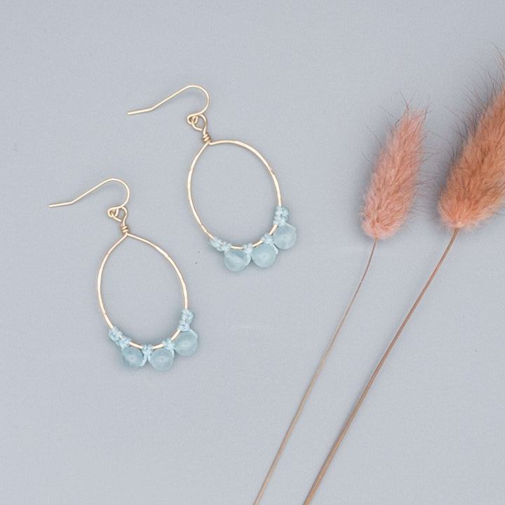 14k gold filled oval hoop earrings with aquamarine beads flat on a gray background